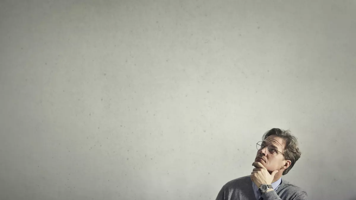 A man is sitting in front of his laptop, looking thoughtful. 