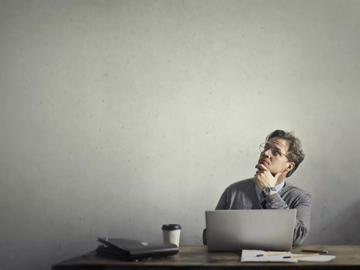 A man is sitting in front of his laptop, looking thoughtful. 