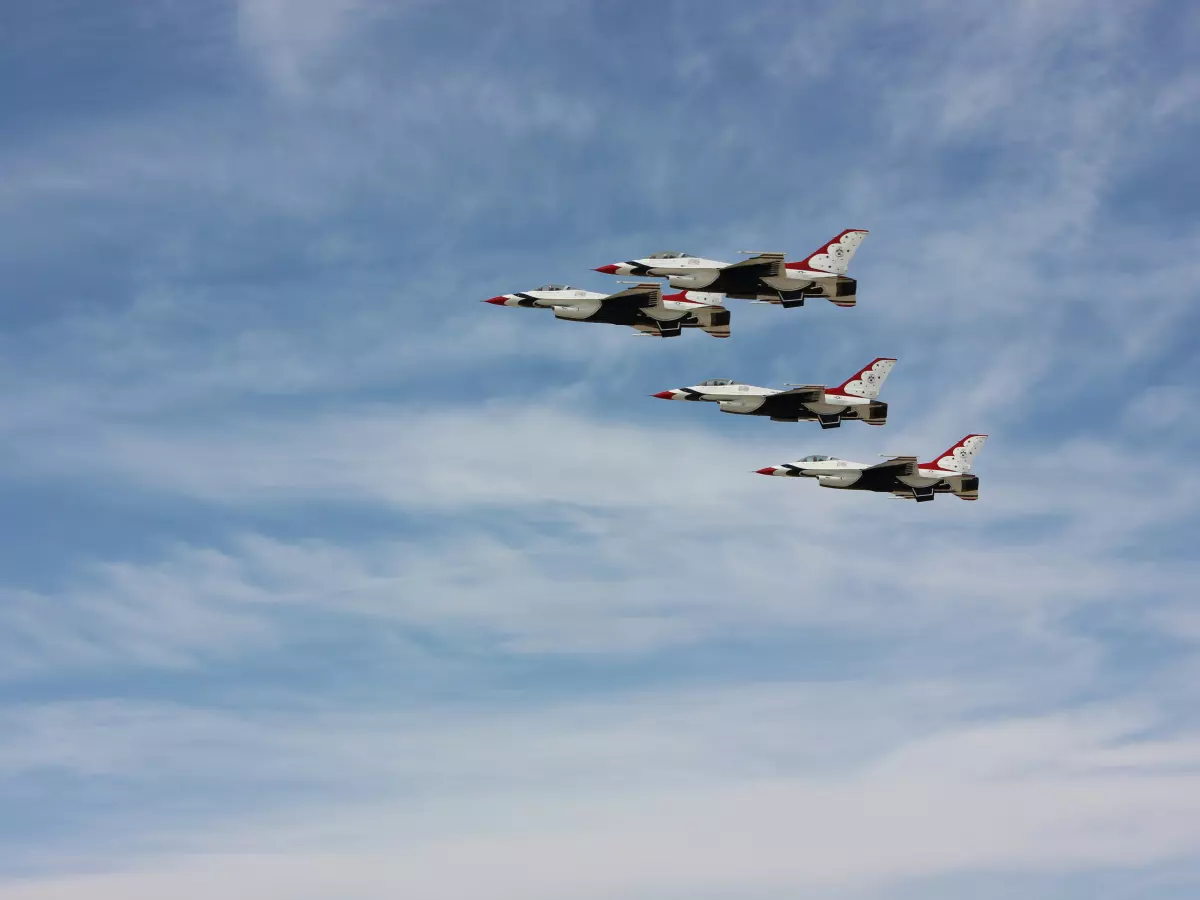 Three white and red airplanes flying in formation against a blue sky with clouds.