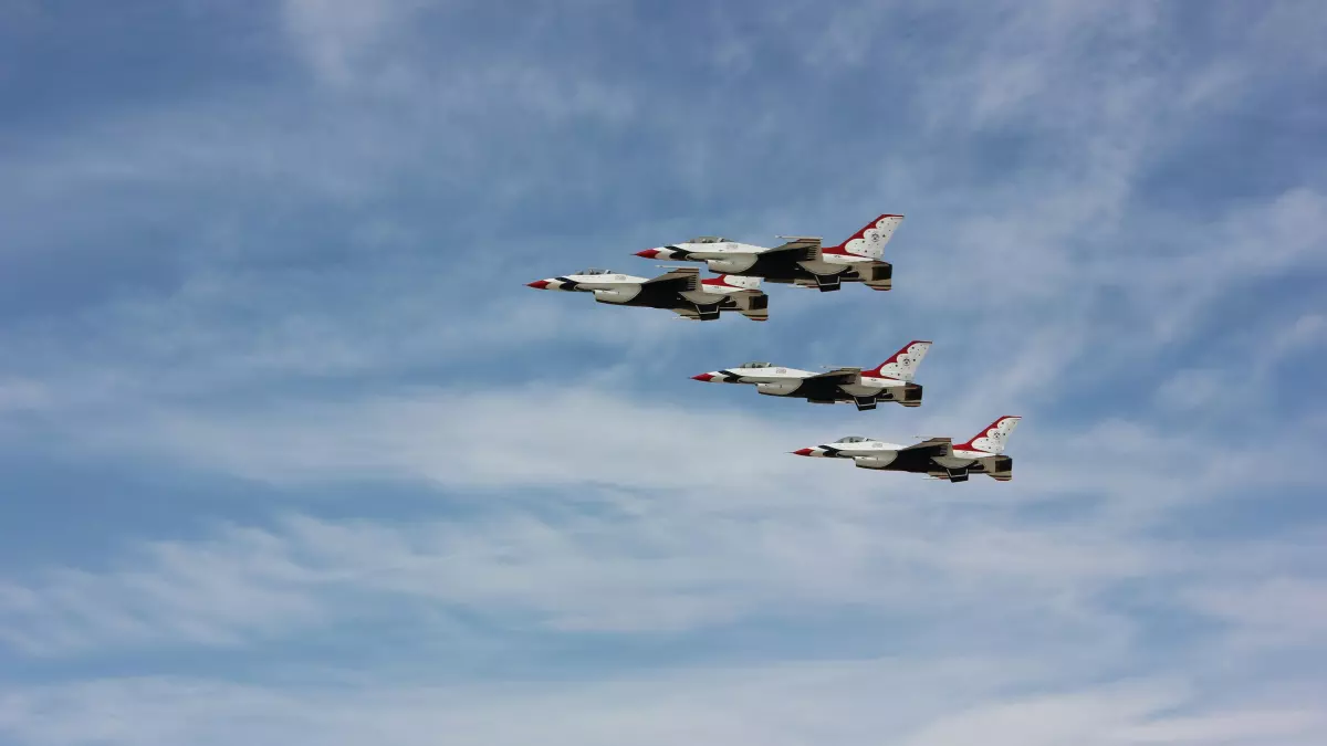 Three white and red airplanes flying in formation against a blue sky with clouds.