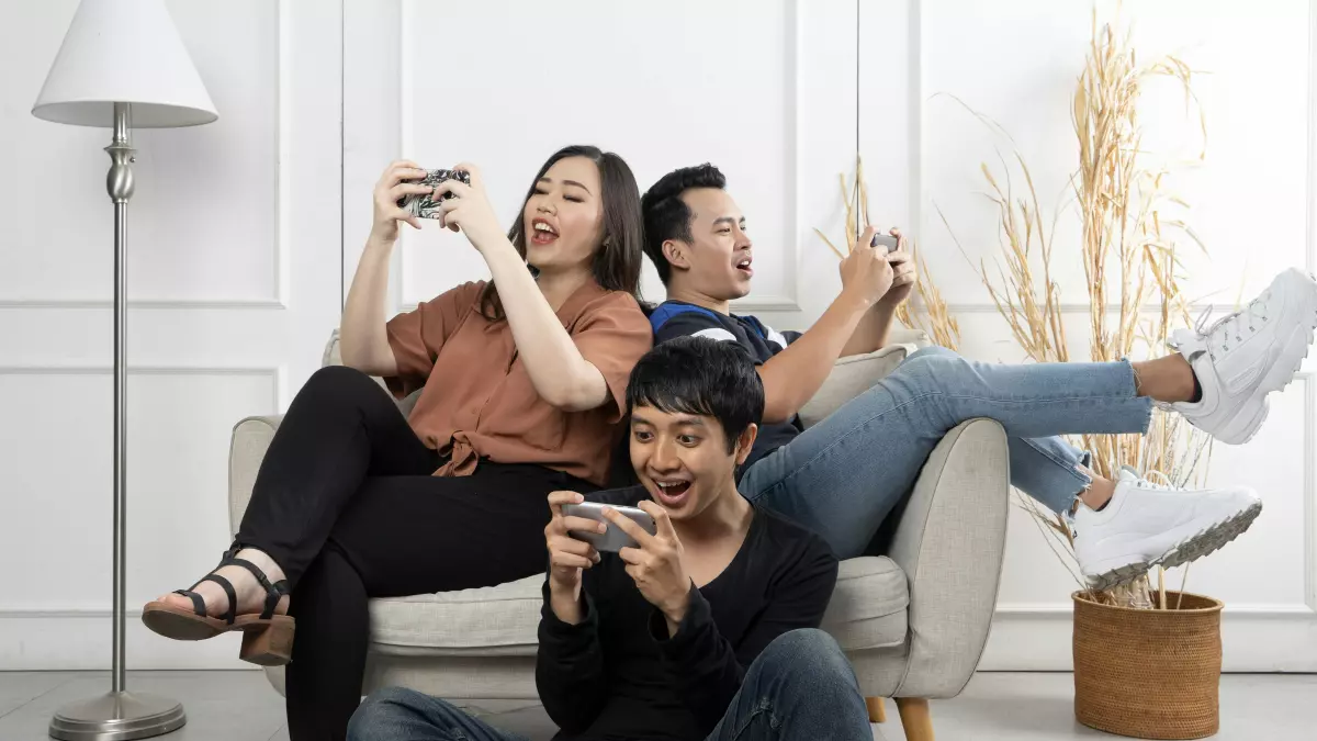 Three people are sitting on a couch and playing games on their smartphones.