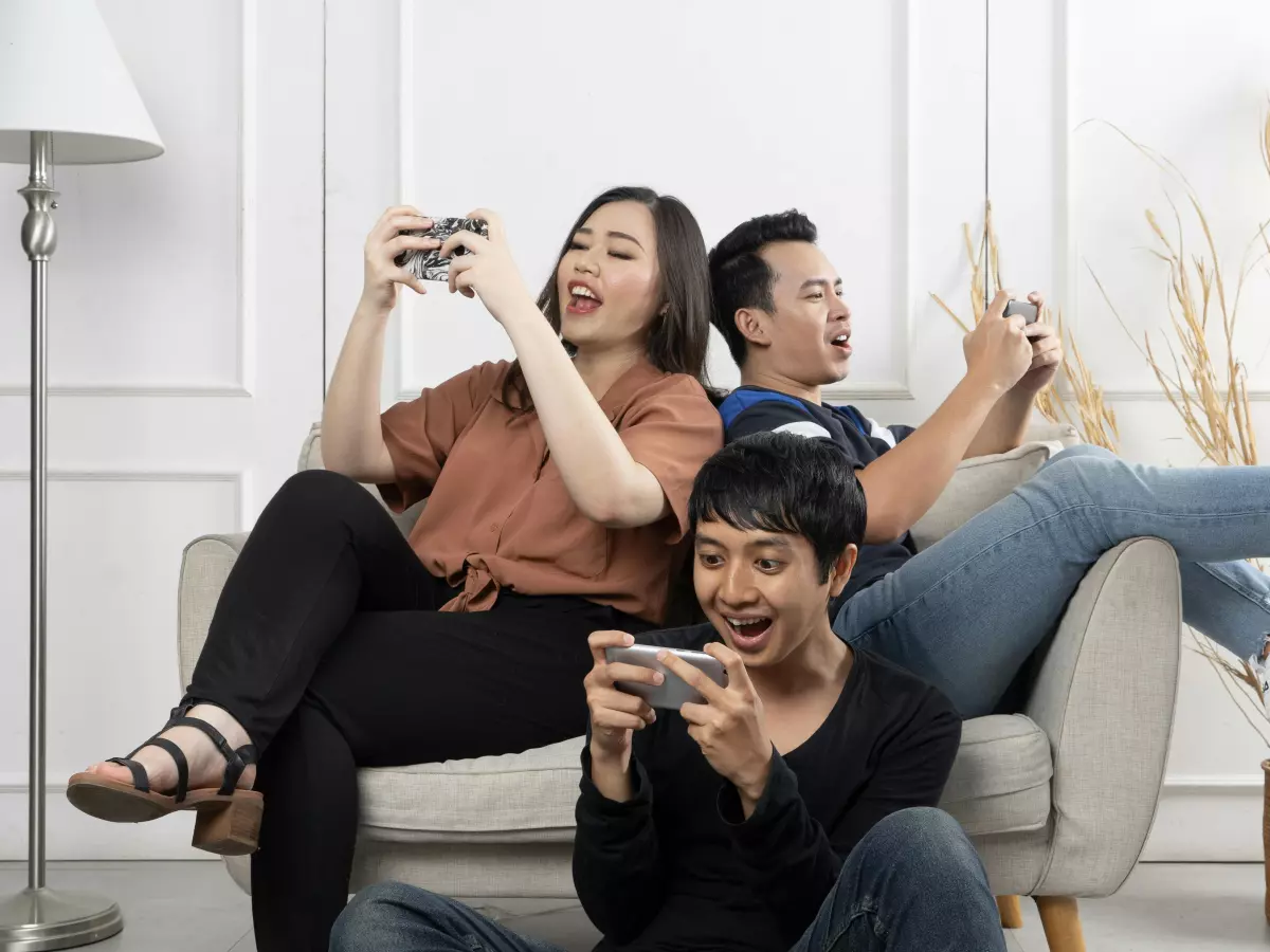 Three people are sitting on a couch and playing games on their smartphones.