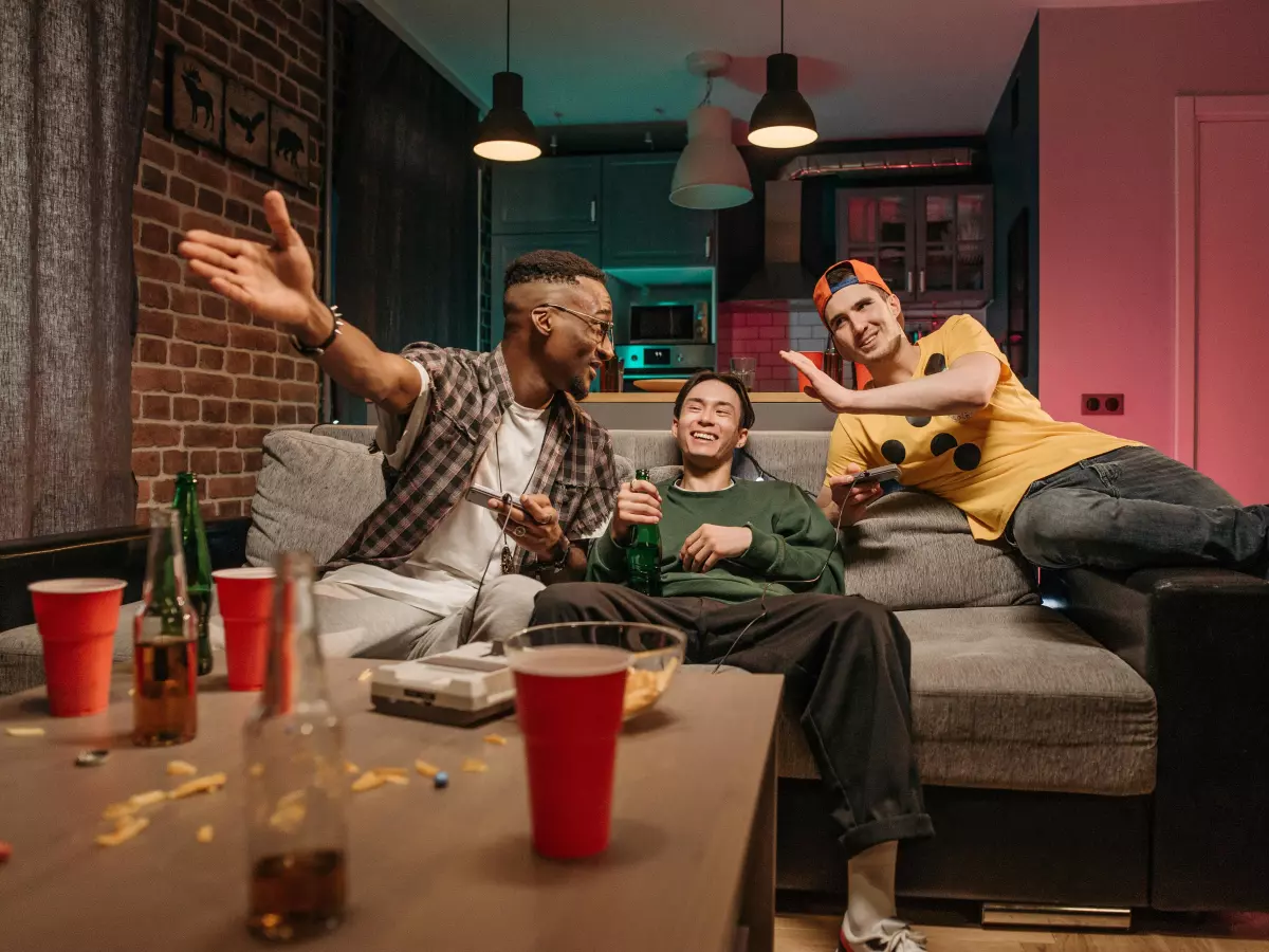 Three friends, one black, one white, one asian, laughing while playing video games.