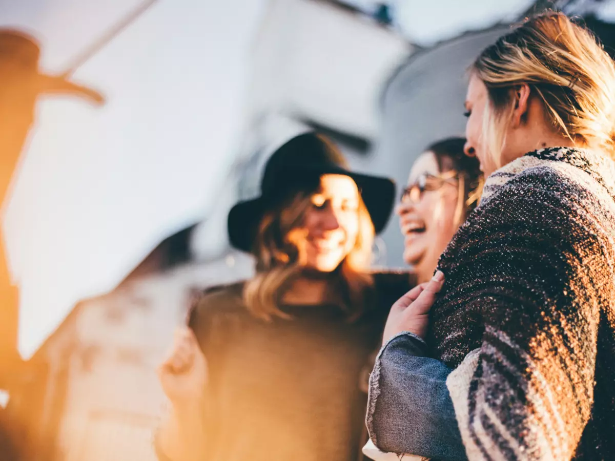 Three women are laughing and talking together outdoors, enjoying each other's company. 