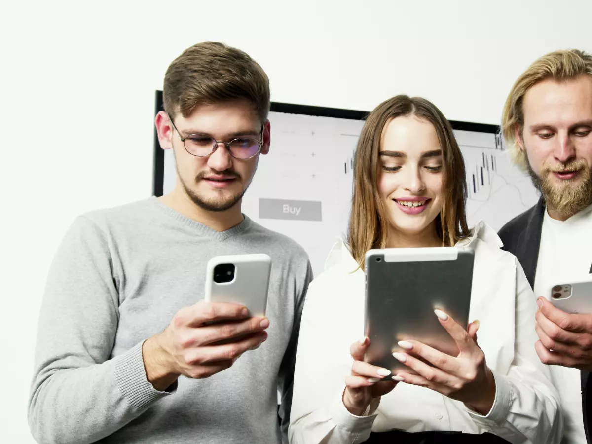 Three people looking at their phones and tablet, with a neutral expression