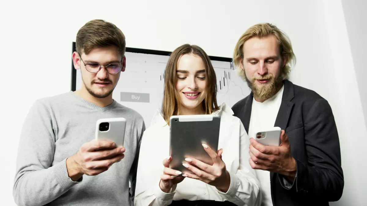 Three people looking at their phones and tablet, with a neutral expression