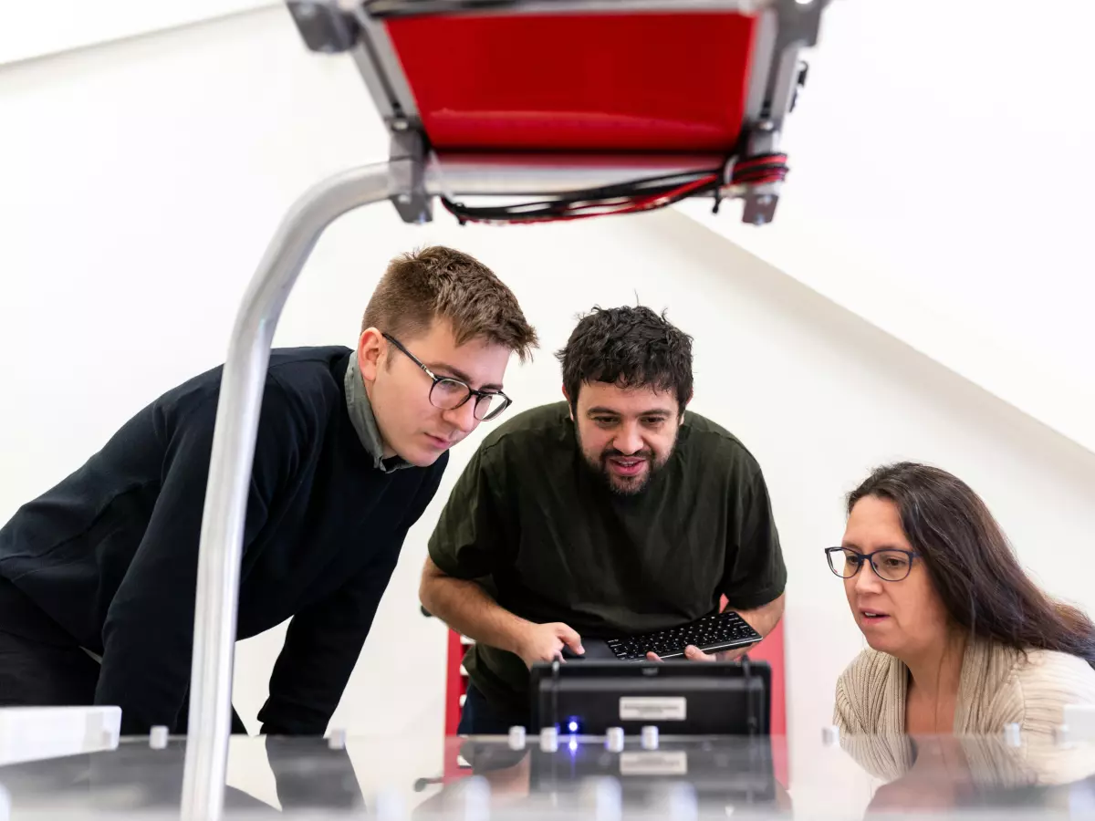 Three people working with a robotic arm in a workspace