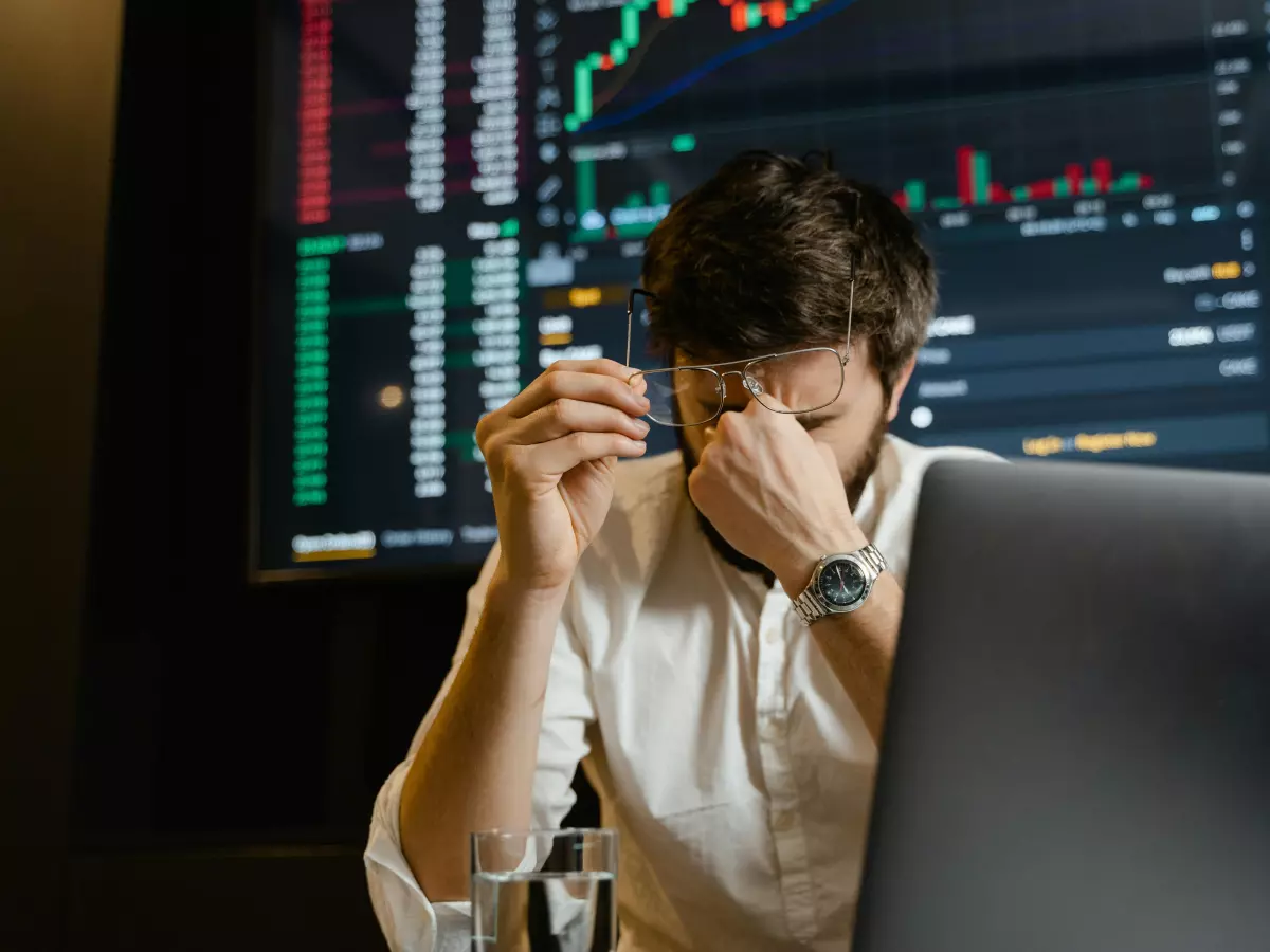 A man sitting in front of a computer screen, looking stressed and holding his head.