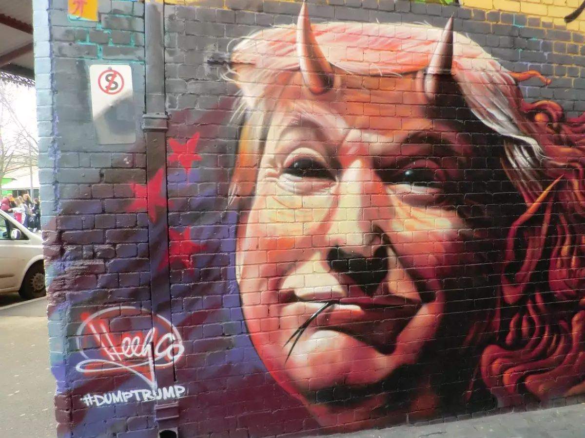 A graffiti mural of Donald Trump with horns on his head, a devilish grin, and the words "#DumpTrump" below.