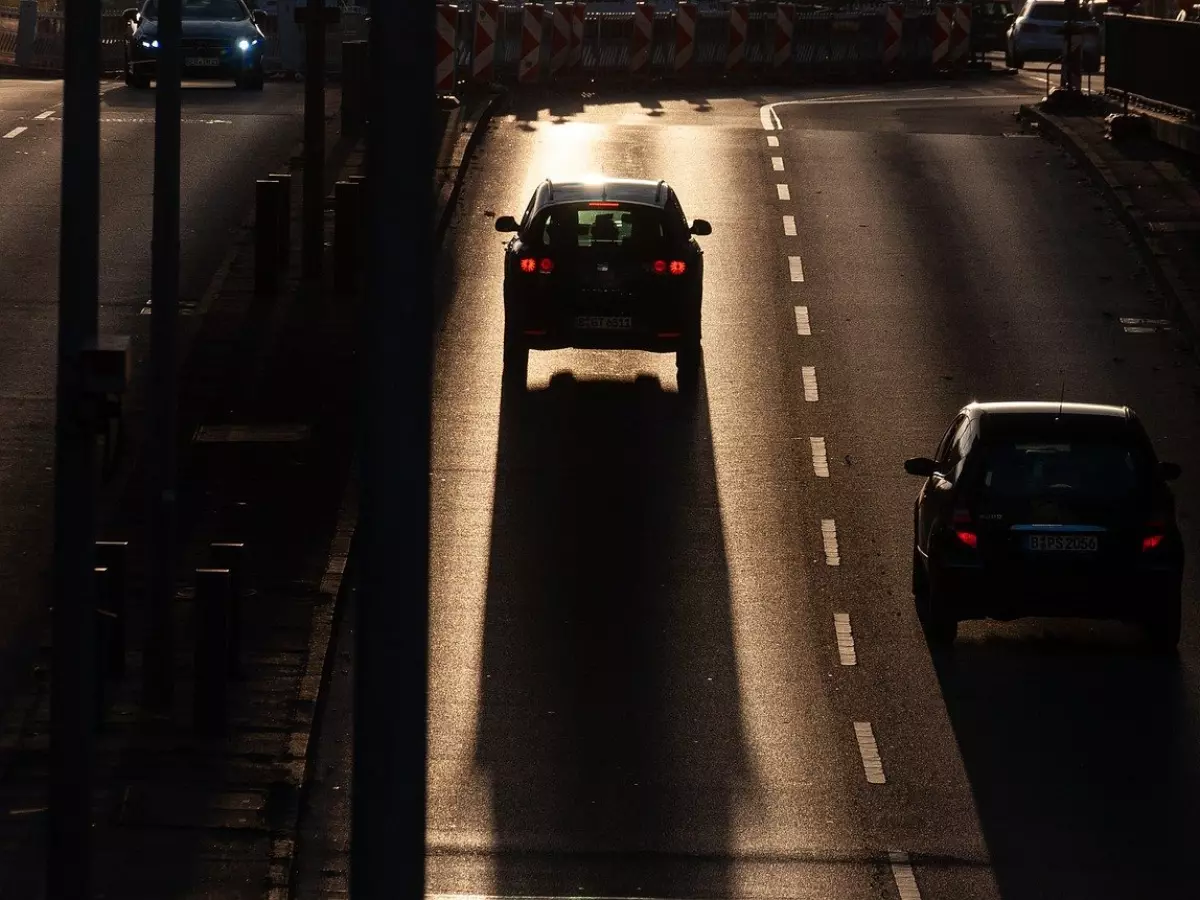 Two cars driving down a road with the setting sun in the background.