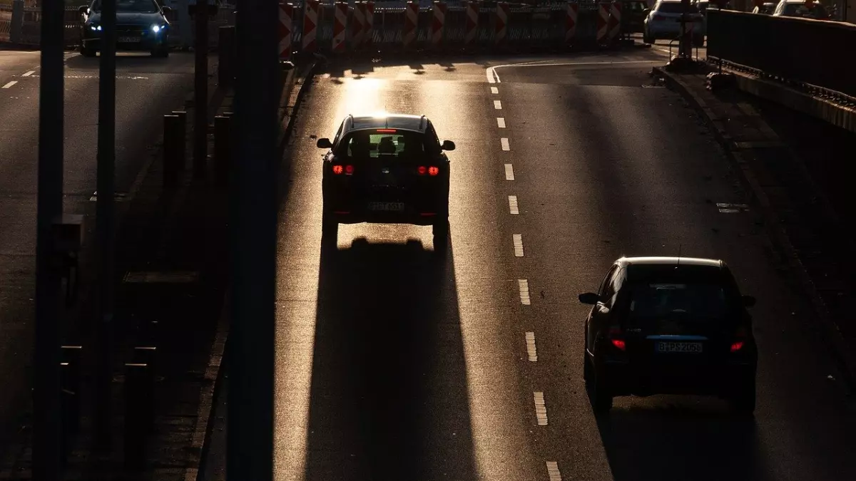 Two cars driving down a road with the setting sun in the background.