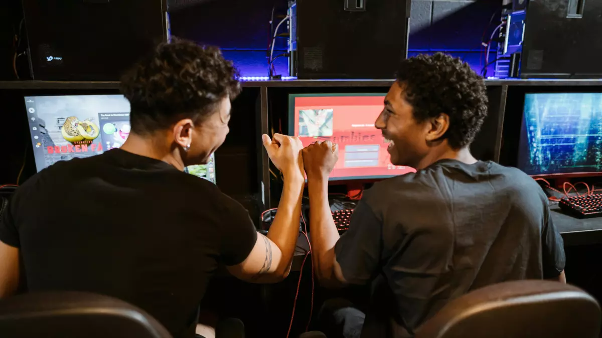 Two young men in a gaming room playing a game on a computer.