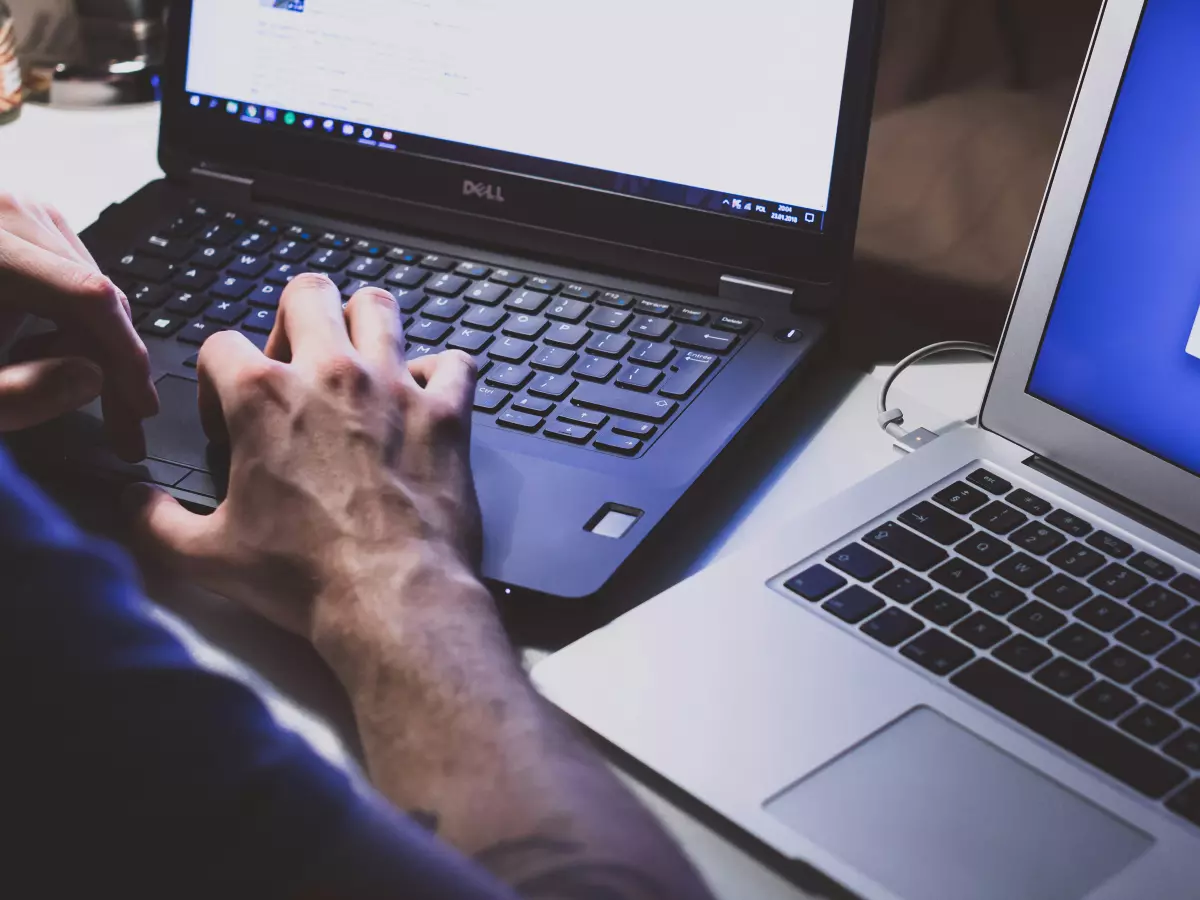 A person's hands typing on a laptop keyboard, with another laptop partially visible in the background.