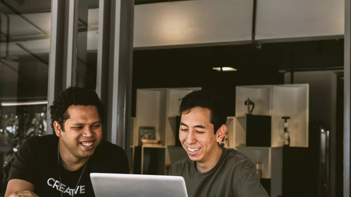 Two young men smiling and looking at a laptop screen.