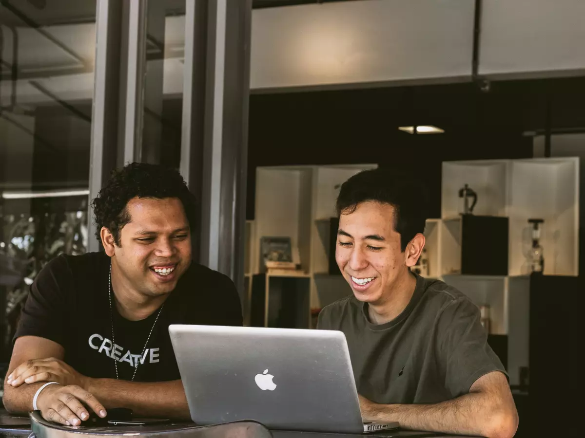 Two young men smiling and looking at a laptop screen.