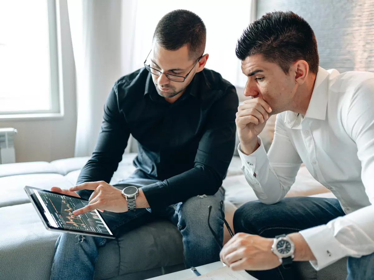 Two men sitting on a bed looking at a tablet.