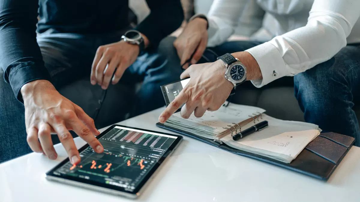 Two people looking at a tablet showing financial data, one is pointing at the screen.