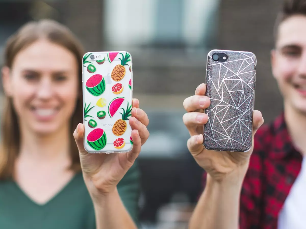 Two young people, a woman and a man, holding their iPhones in protective cases, smiling and looking at the camera.