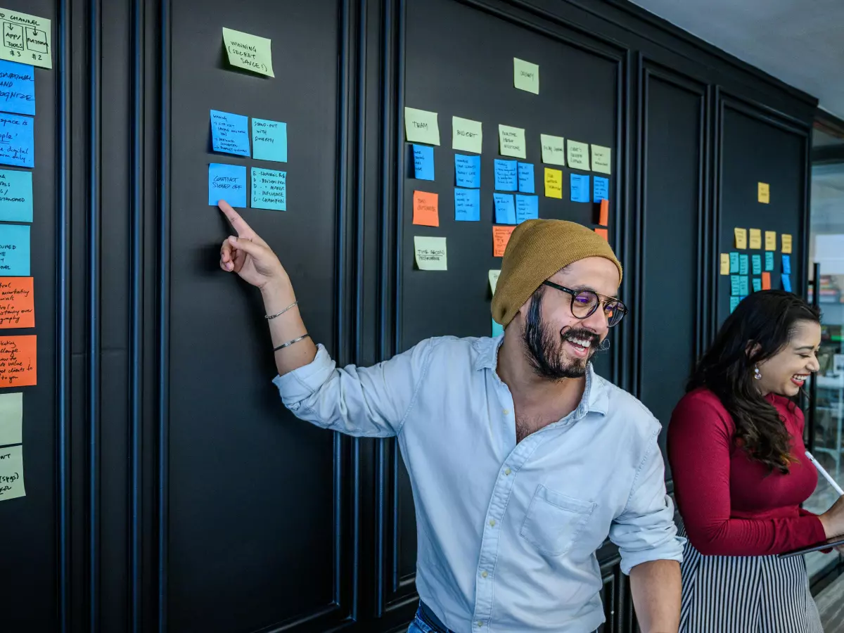 Two people are working together on a project using sticky notes on a wall.