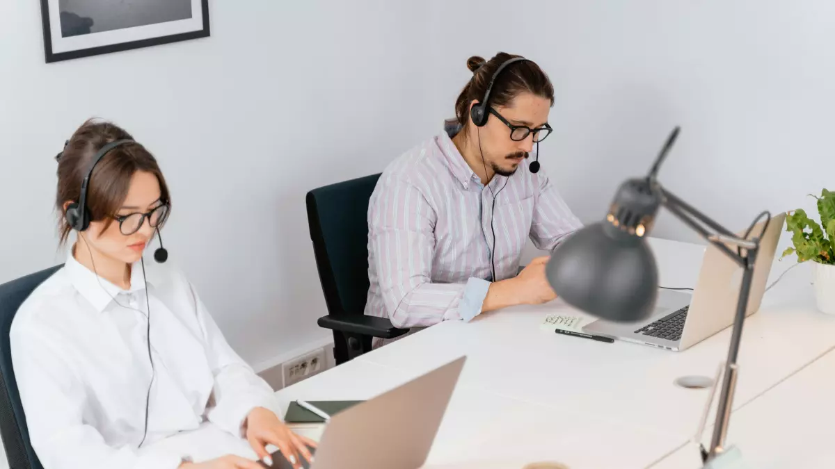 Two people are working on laptops at a desk.