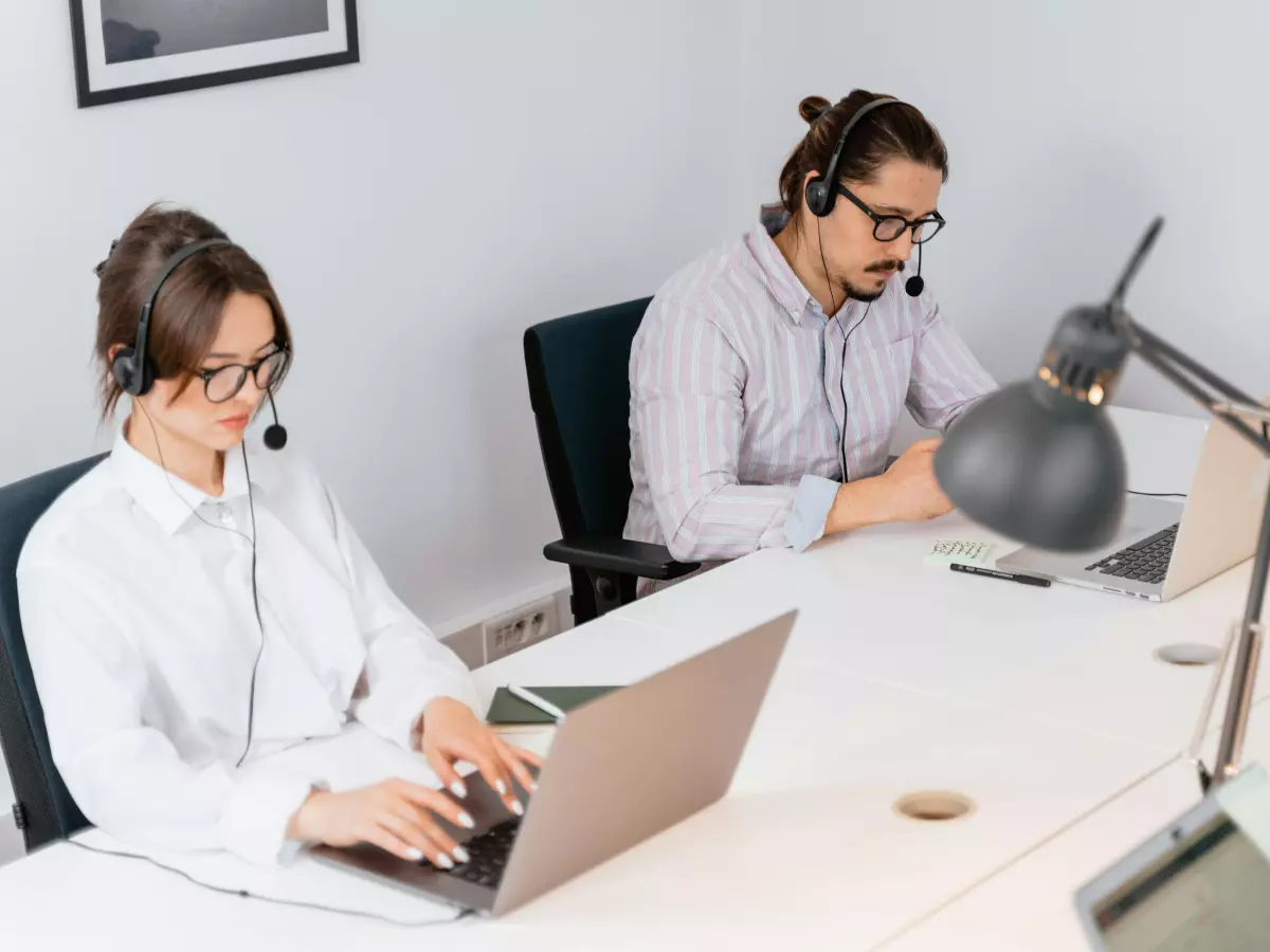 Two people are working on laptops at a desk.