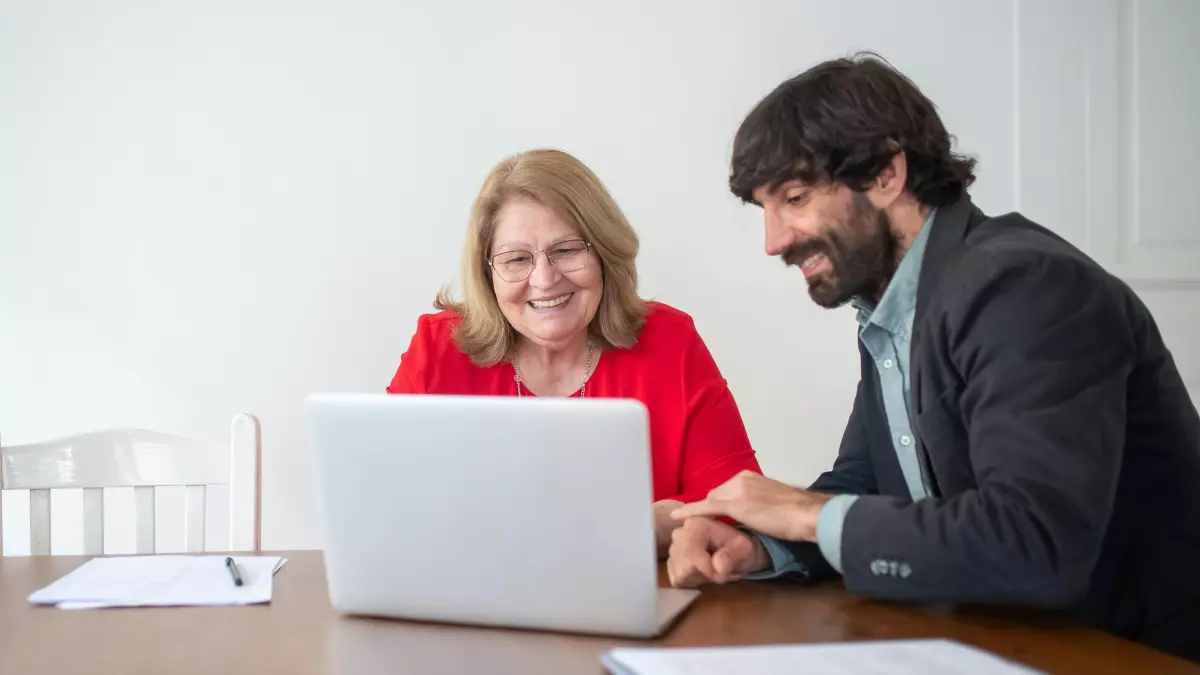 A man and a woman are looking at a laptop computer. The woman is pointing at the screen.