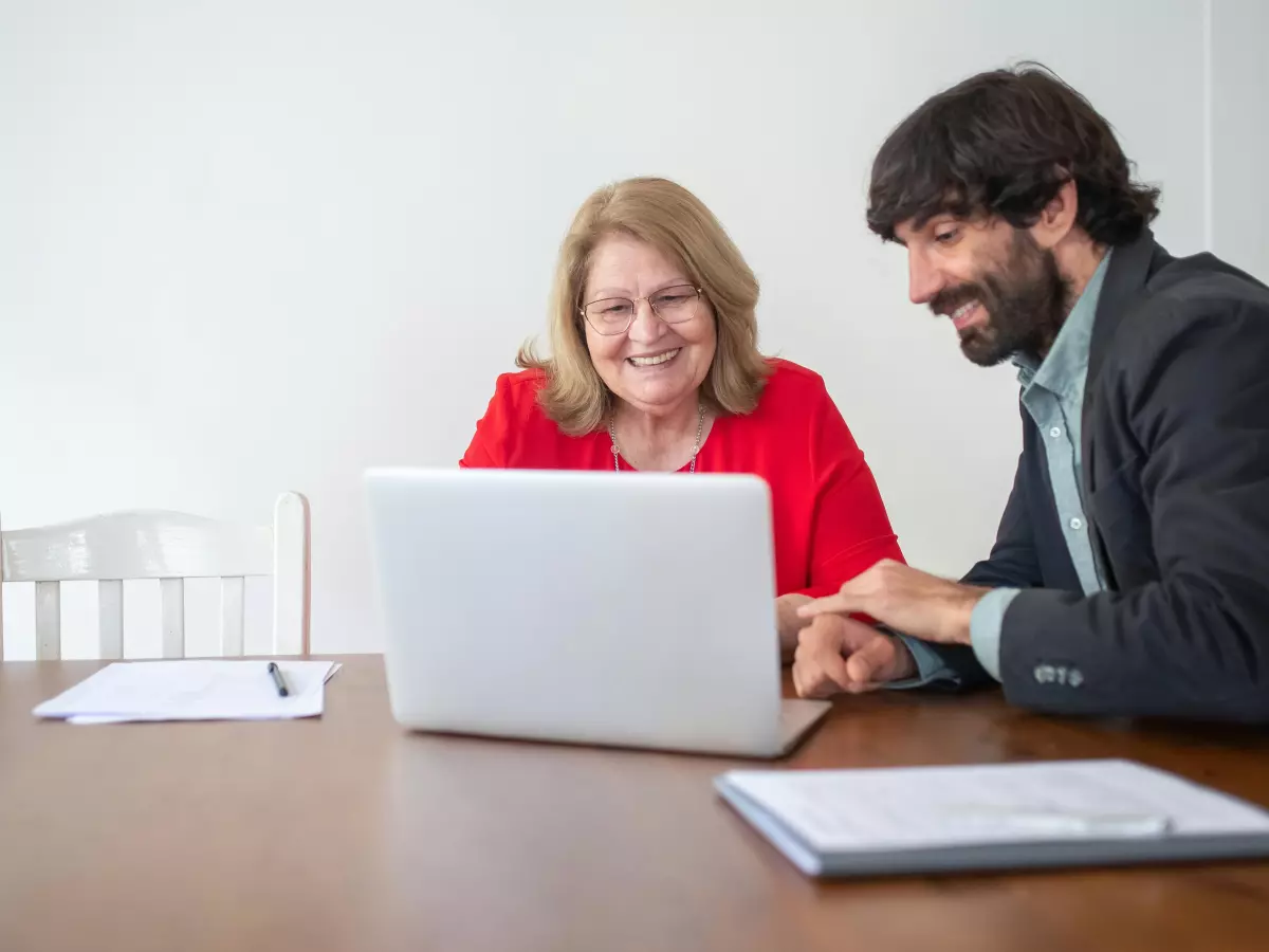 A man and a woman are looking at a laptop computer. The woman is pointing at the screen.