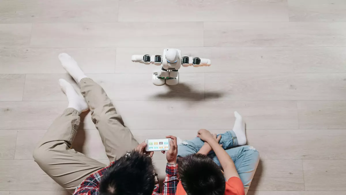 A white robot is sitting on a wooden floor. A man and a boy are sitting in front of the robot.