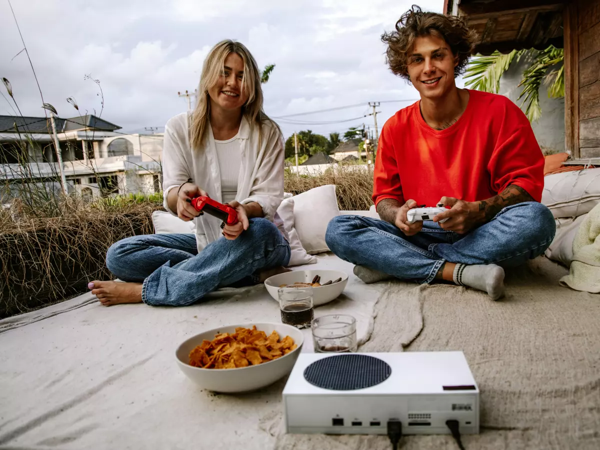 Two people are sitting on a blanket, playing video games on a console.