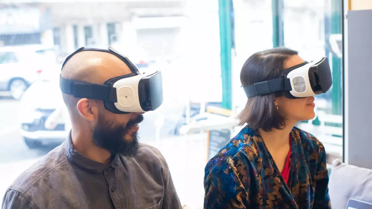 Two people wearing VR headsets, one with a beard and one with long dark hair, looking up in wonder.