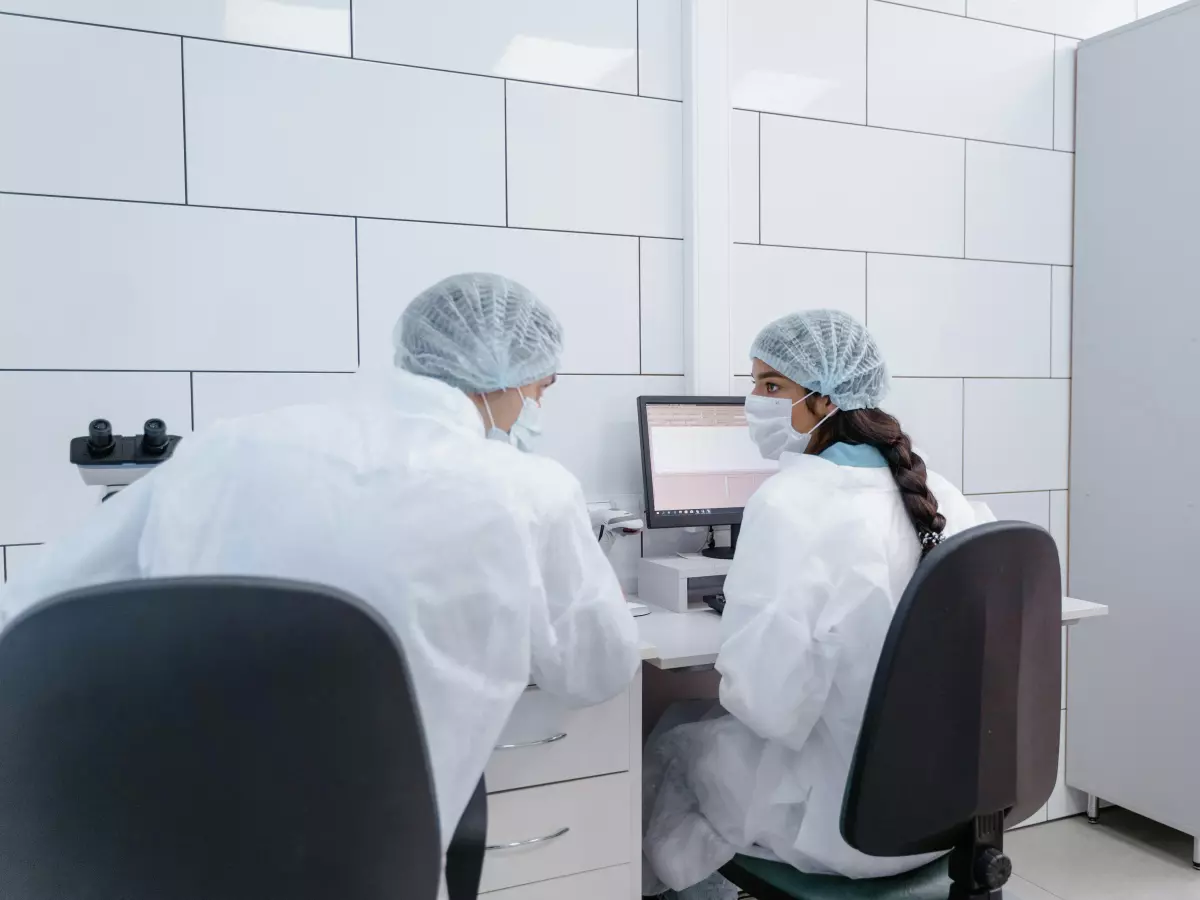 Two people in lab coats are sitting at a computer, looking at a screen with graphs.