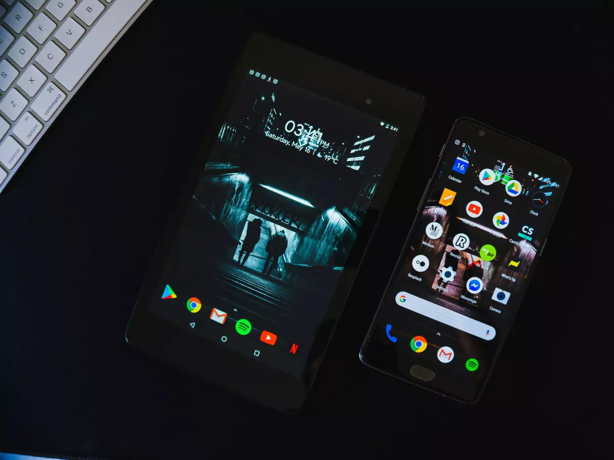 Two Android devices, one a tablet, the other a smartphone, both have dark backgrounds, apps are visible on the smartphone.