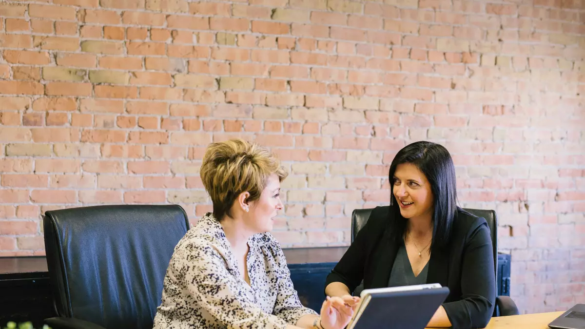 Two women in a professional setting discussing something on a tablet