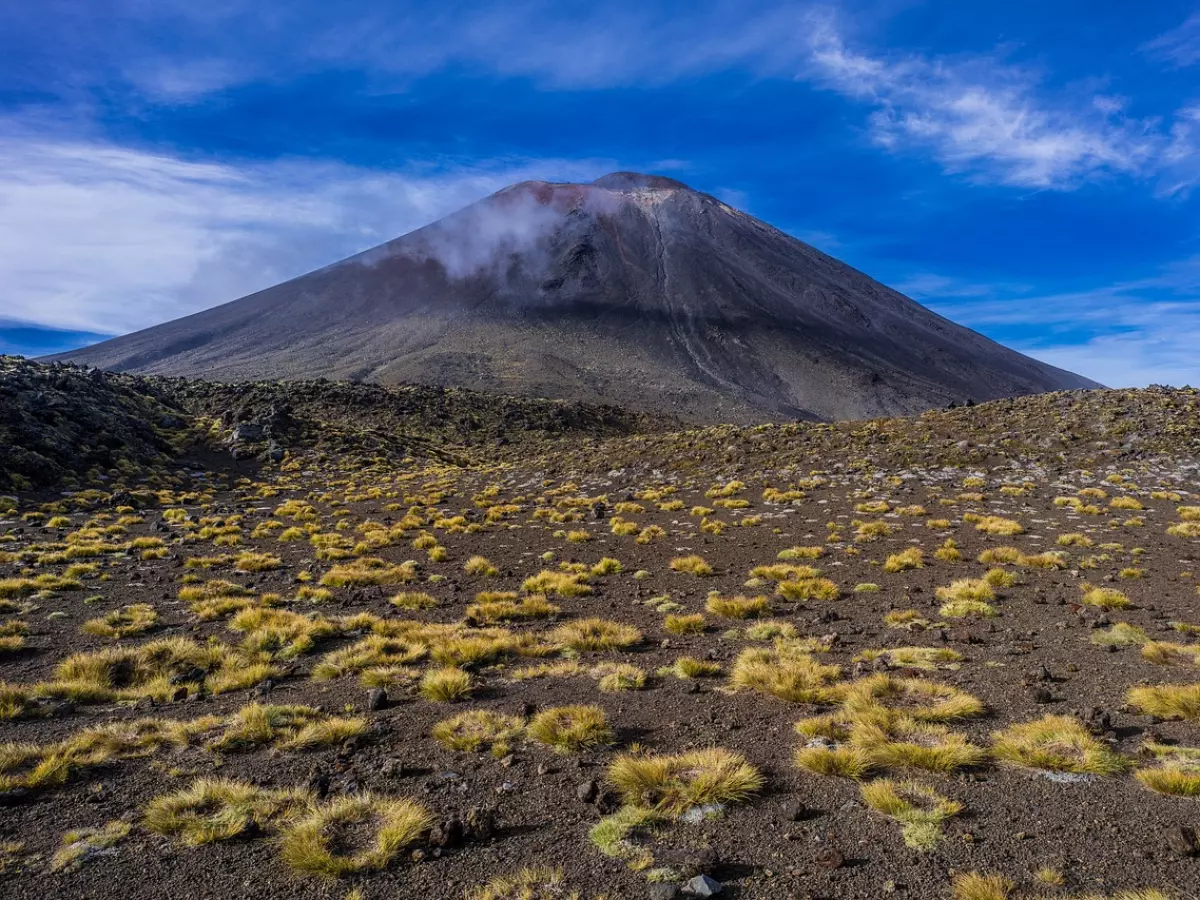 A photo of a volcano with a blue sky and some clouds in the background