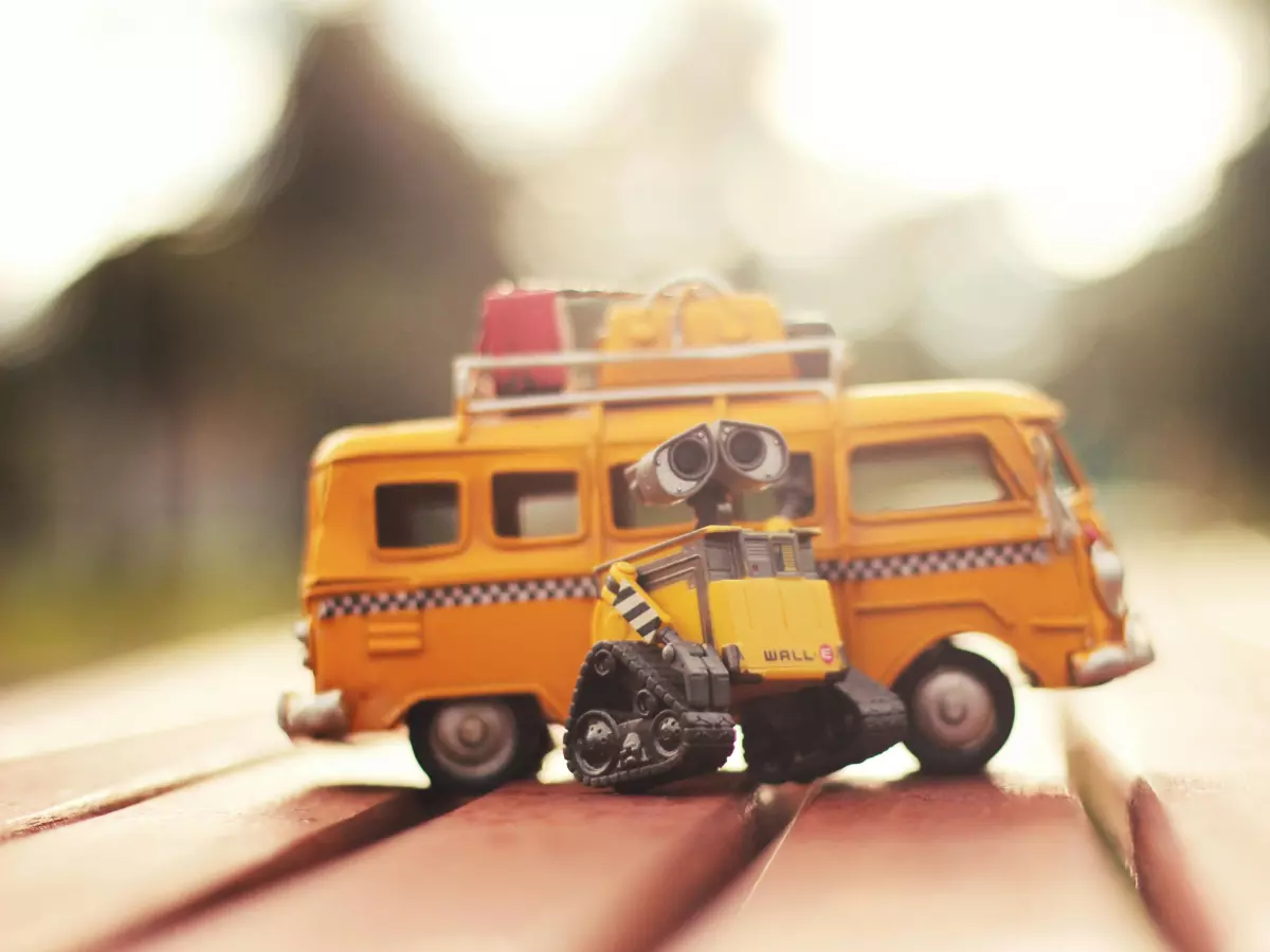 A small robot driving a yellow toy van. The image has a whimsical and colorful feel.