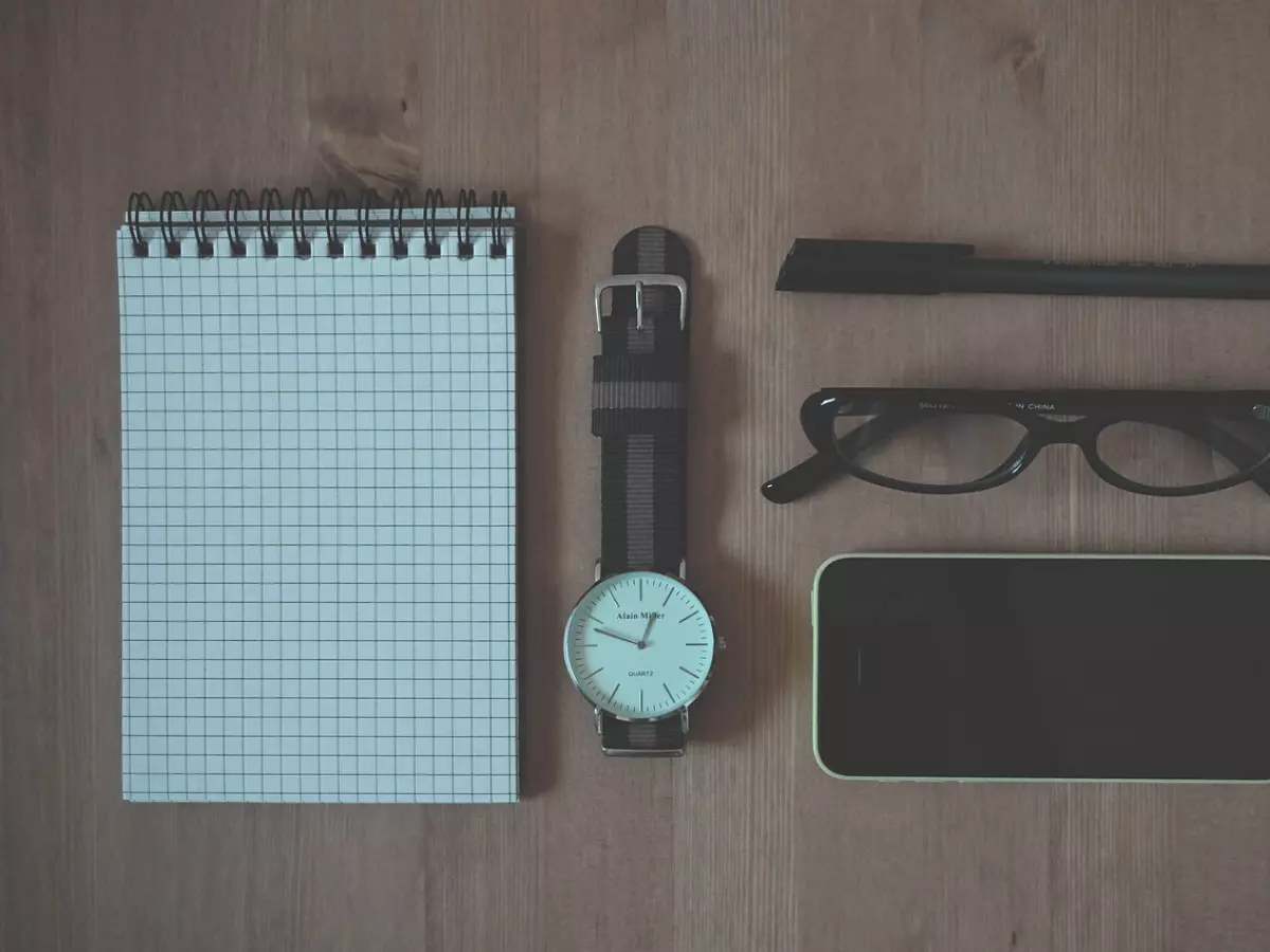 A flat lay of a notebook, pen, glasses, watch and a phone