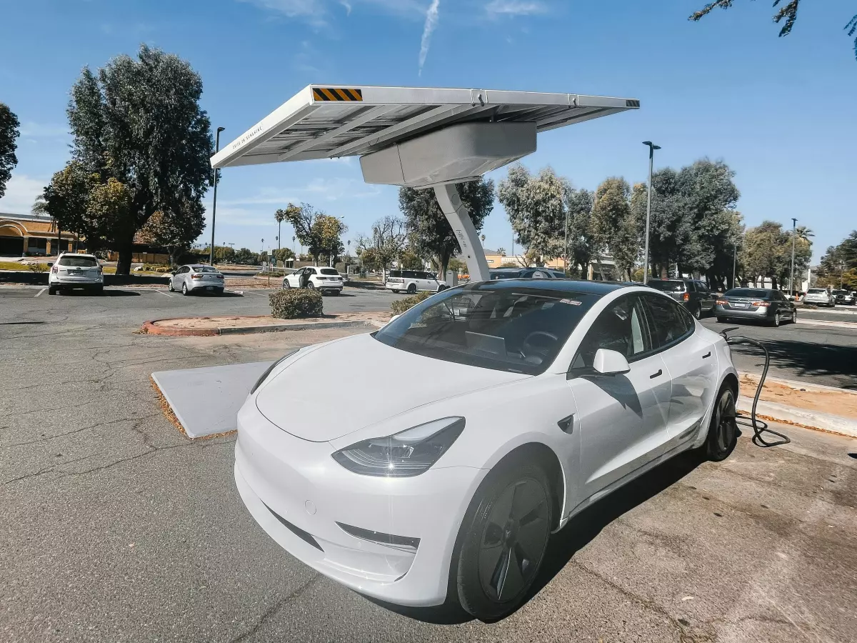 A white Tesla Model 3 is plugged into a charging station under a solar panel.