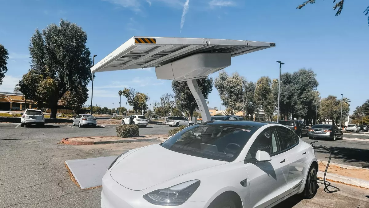 A white Tesla Model 3 is plugged into a charging station under a solar panel.