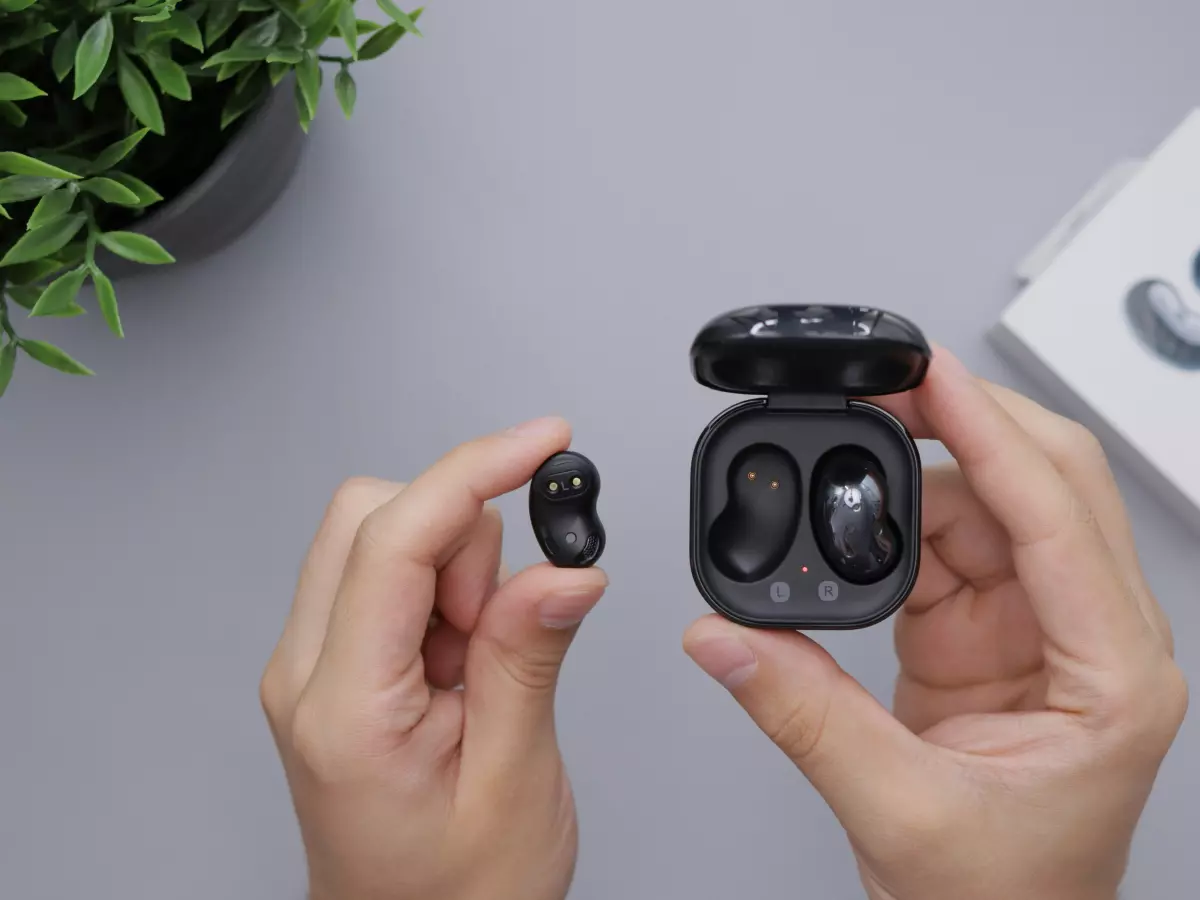 A pair of black Samsung Galaxy Buds 3 earbuds are being held by a hand. The charging case is open and the earbuds are clearly visible.