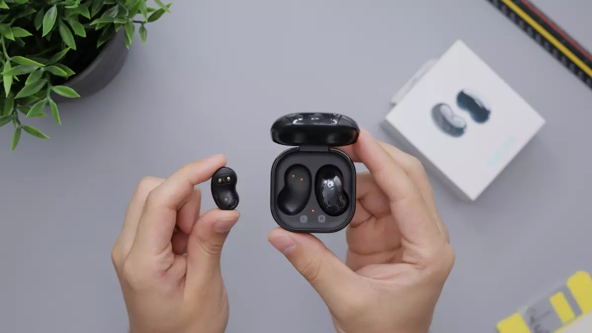 A pair of black Samsung Galaxy Buds 3 earbuds are being held by a hand. The charging case is open and the earbuds are clearly visible.