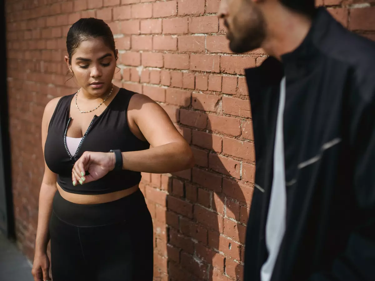 A young woman in athletic wear checking her smartwatch during a workout in a city alley.