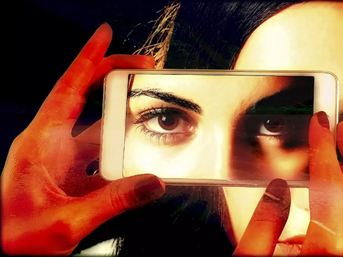 A woman's eyes looking at the camera but the reflection in her phone shows another woman's eyes.