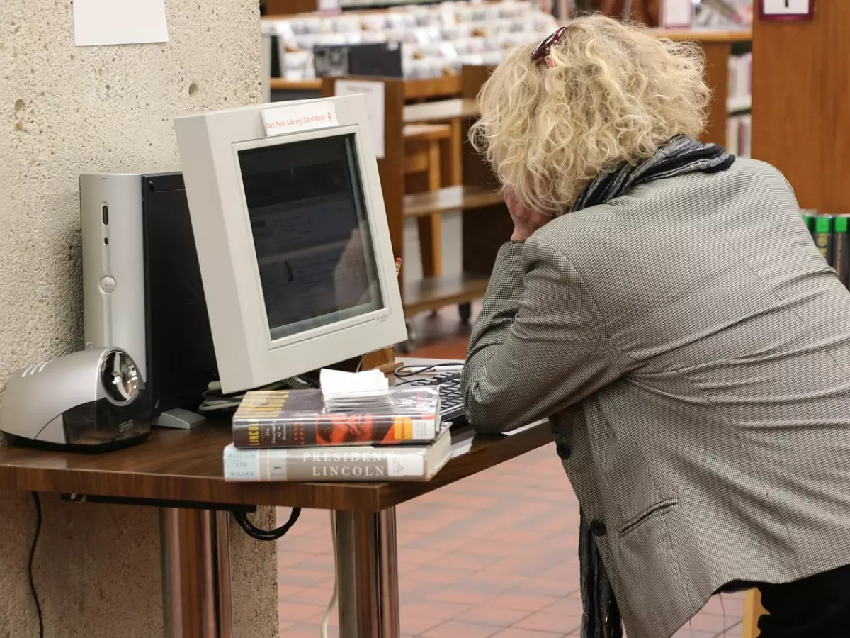 A woman in a library is using a desktop computer.