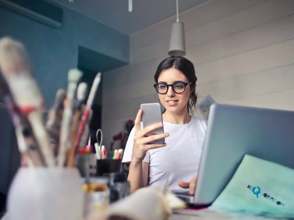 A woman using a phone at a desk with a laptop