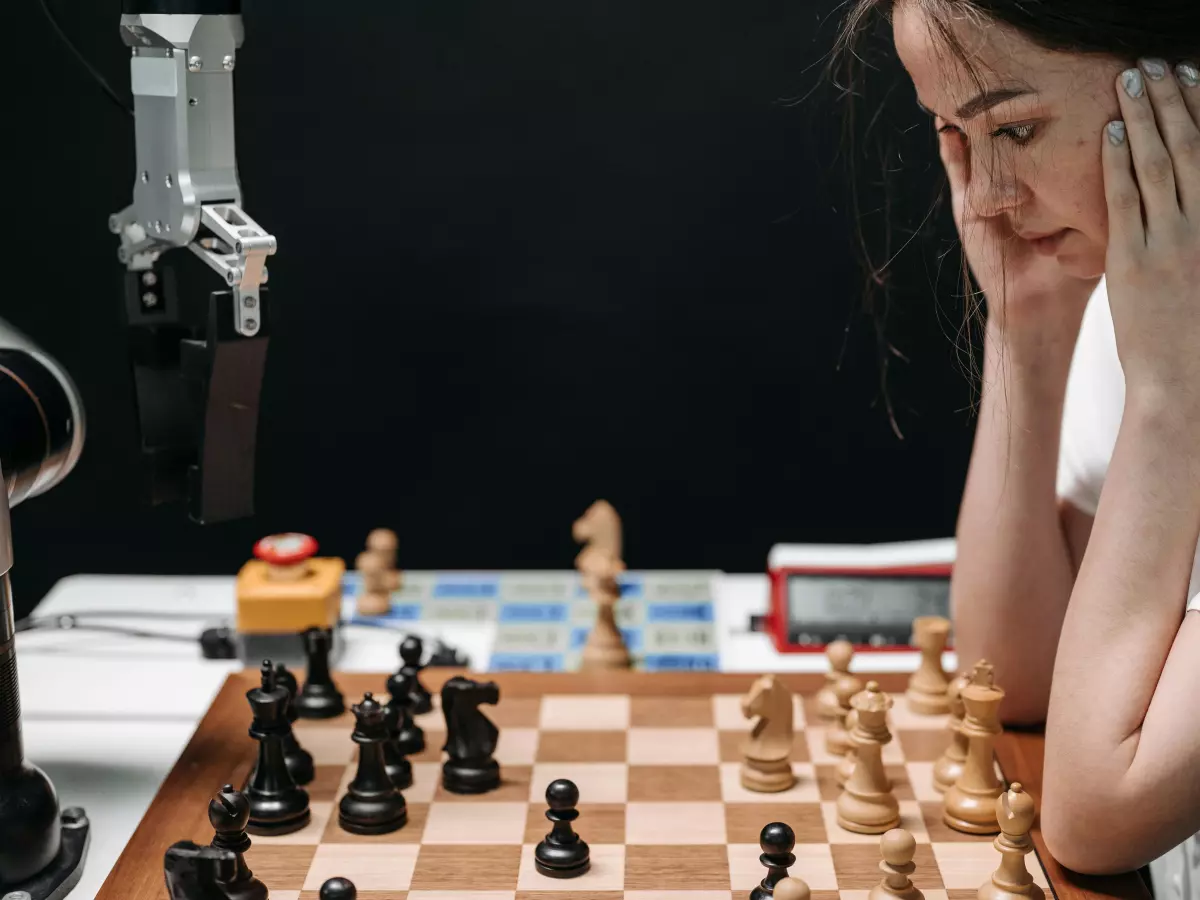 A woman playing chess against a robotic arm. She looks concerned as if she is losing the game.