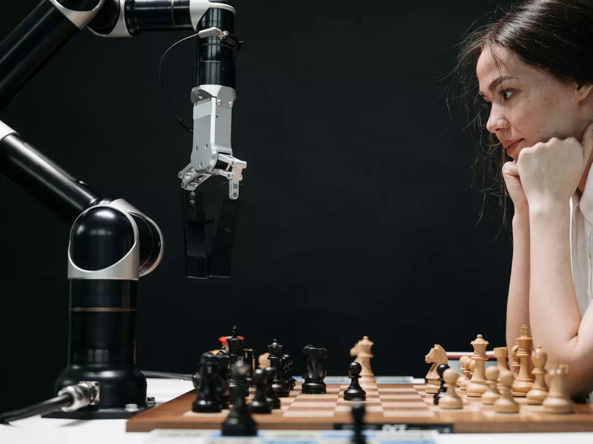 A close-up shot of a humanoid robot arm playing chess against a human opponent.