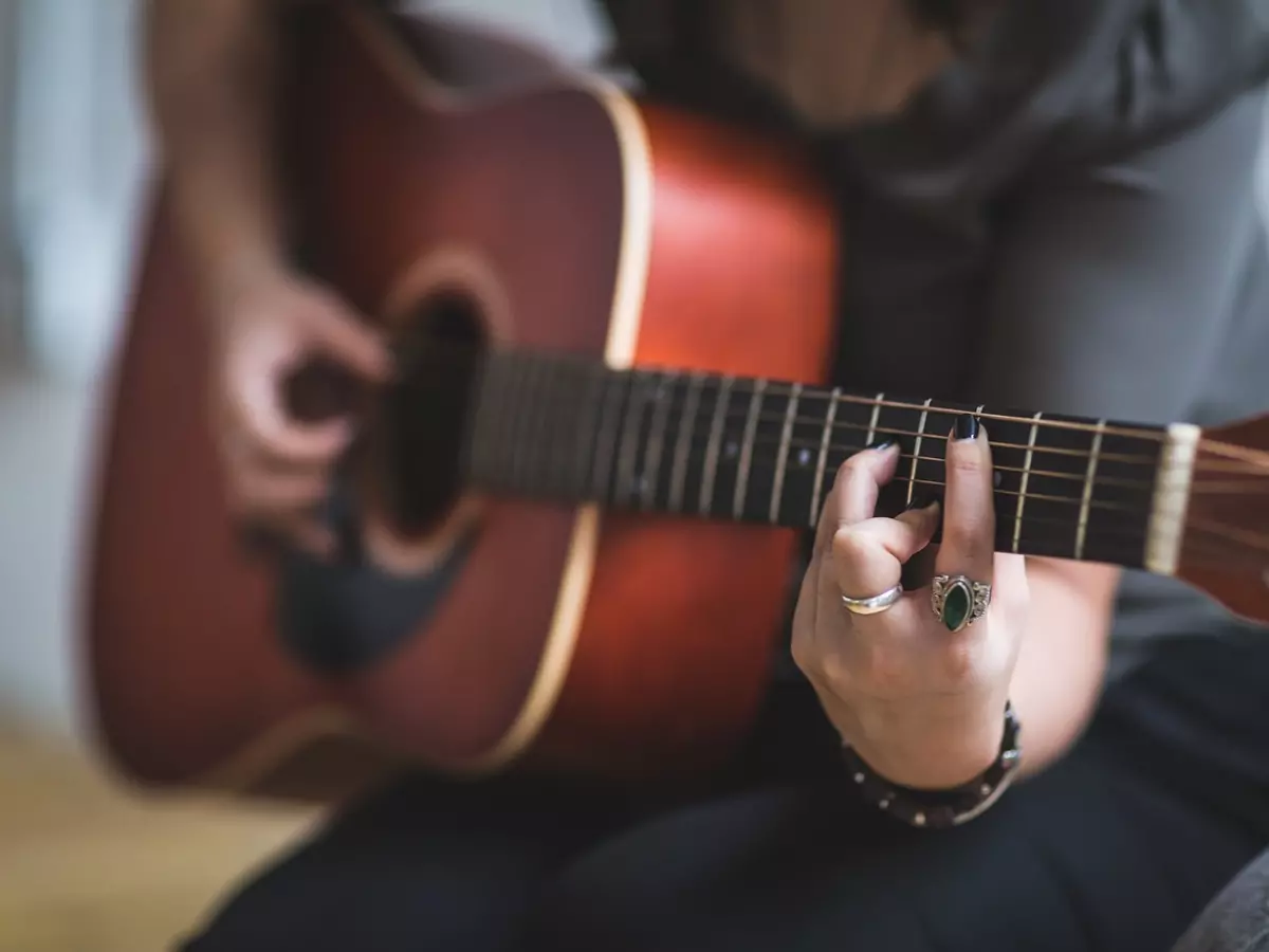 A hand playing a guitar with a green smart ring on the finger.