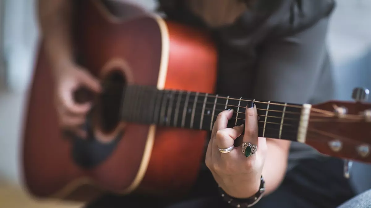 A hand playing a guitar with a green smart ring on the finger.