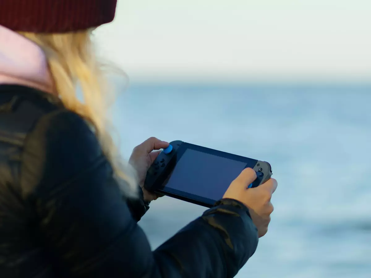 A woman is playing a game on a handheld device while standing on a beach.