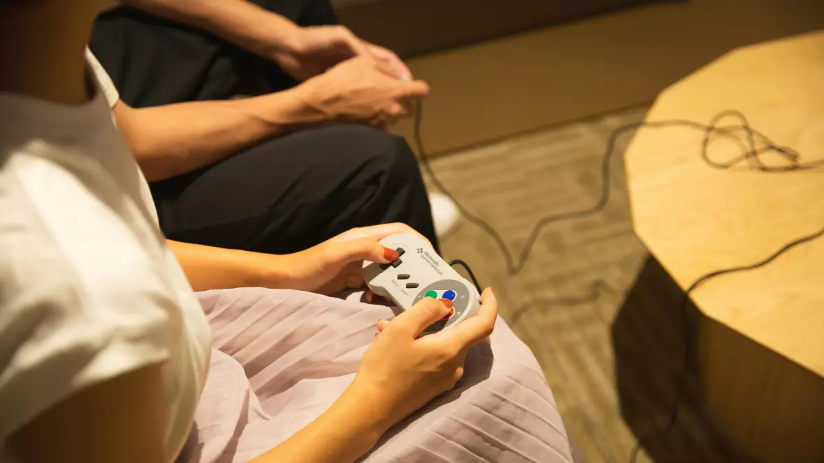 A person playing a retro game with a handheld console, the person is wearing a white shirt and a pink skirt, the background is blurred and the focus is on the person